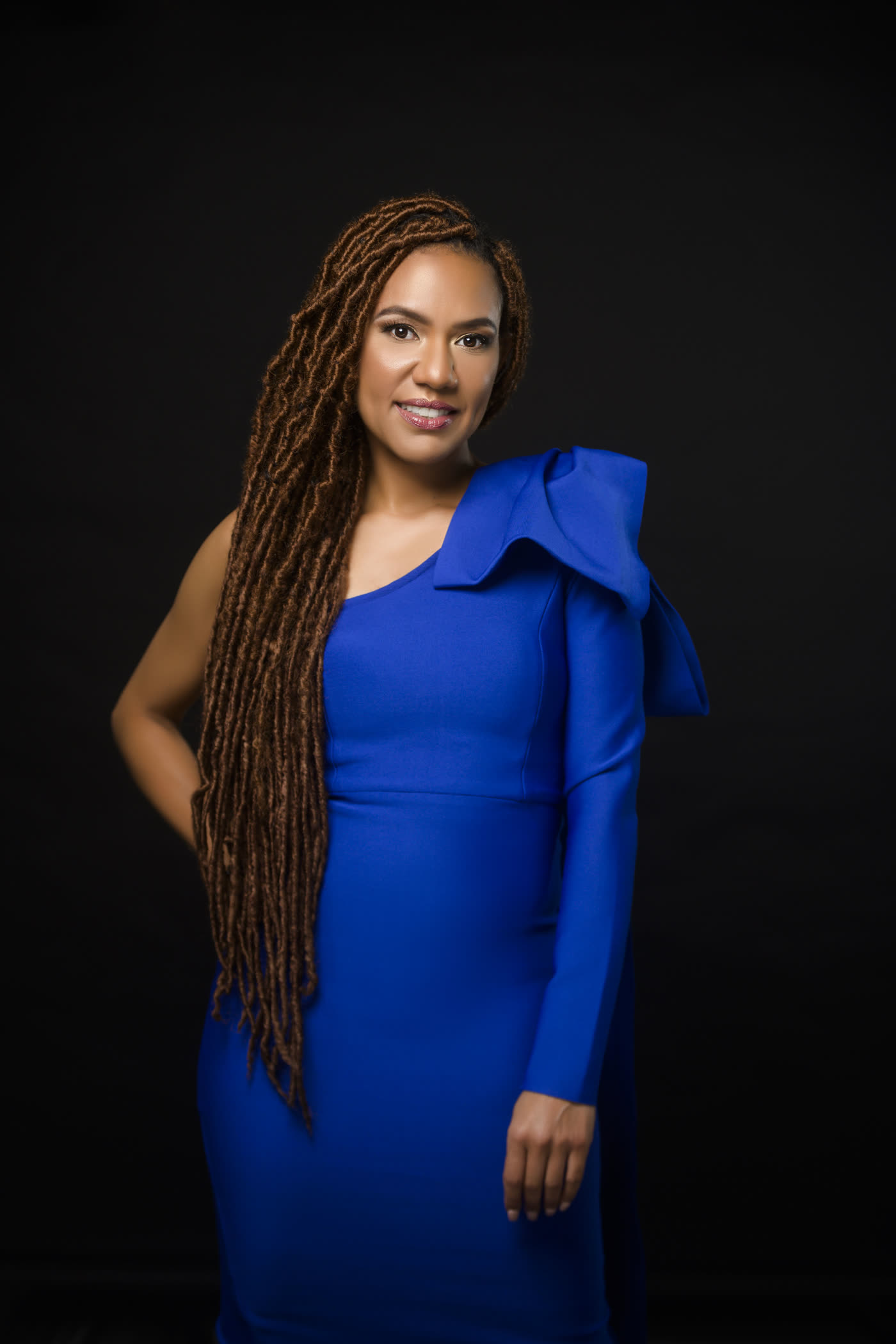 A Hyphy Hippie owner in a blue one-shoulder dress against a dark backdrop